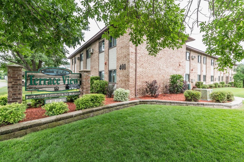 the front of a brick building with a green lawn and a sign that reads farmers
