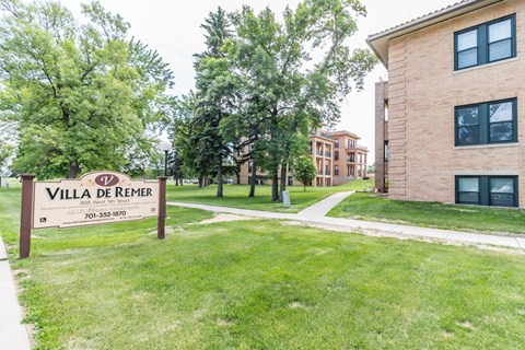 A sign for Villa de Remer stands in a grassy area in front of a building.