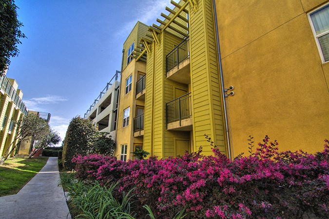 a yellow apartment building with a sidewalk and colorful flowers