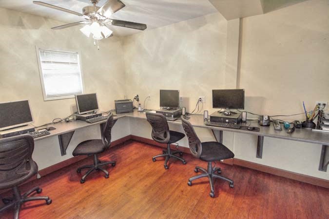 a room with three desks with computers and a ceiling fan