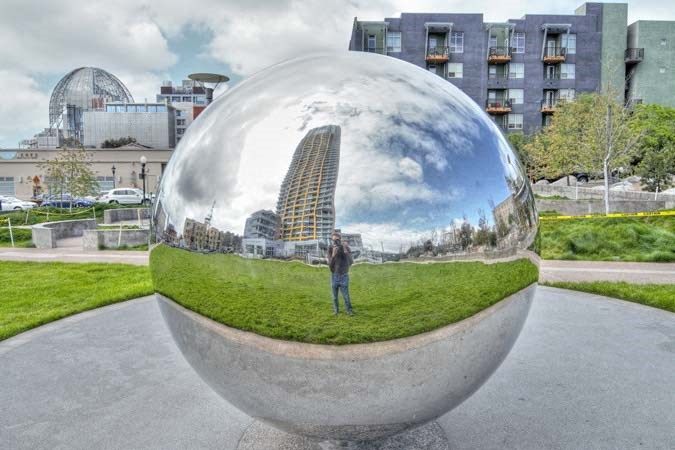 a man taking a picture of himself in a glass ball in a park
