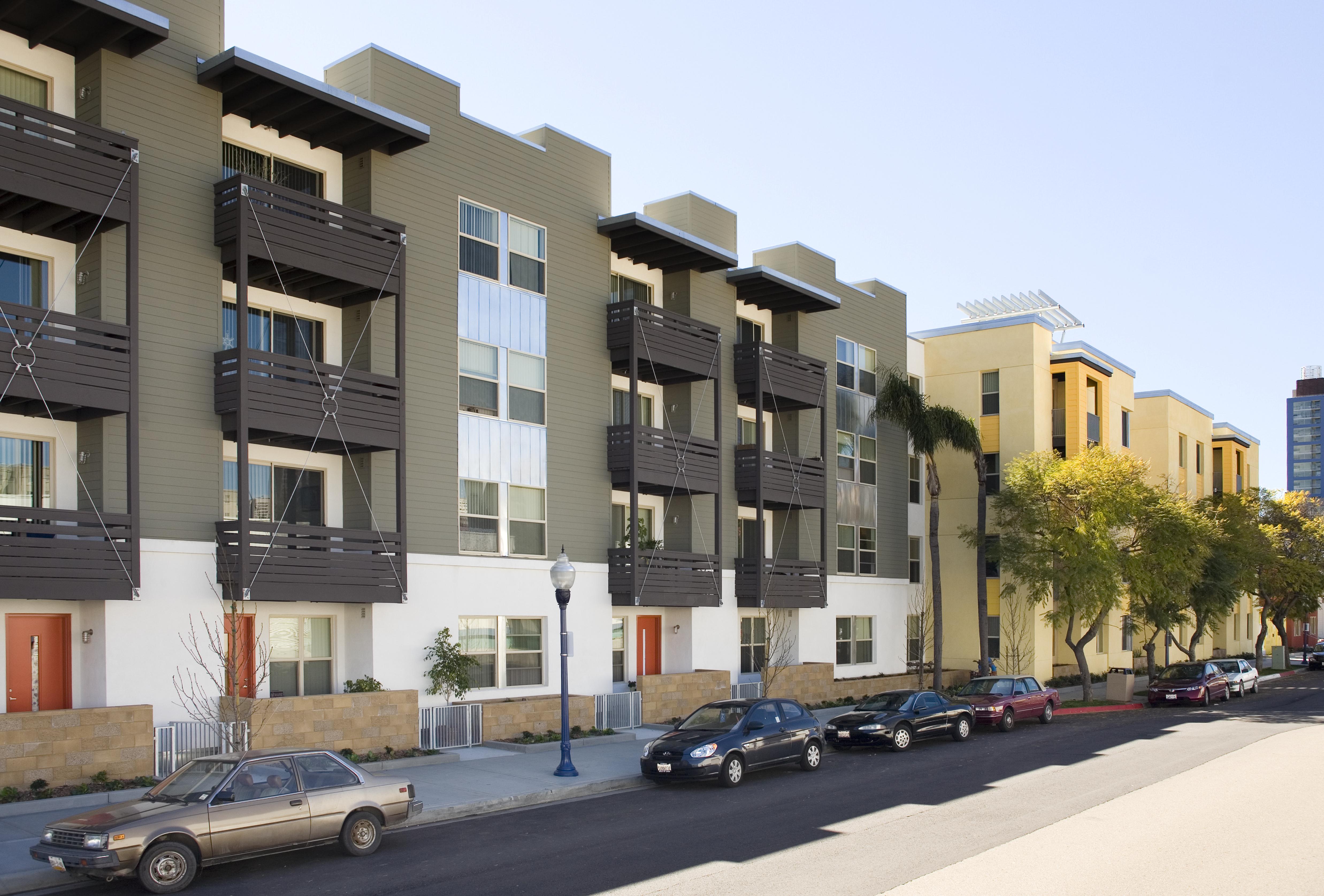 A row of apartment buildings with cars parked in front.