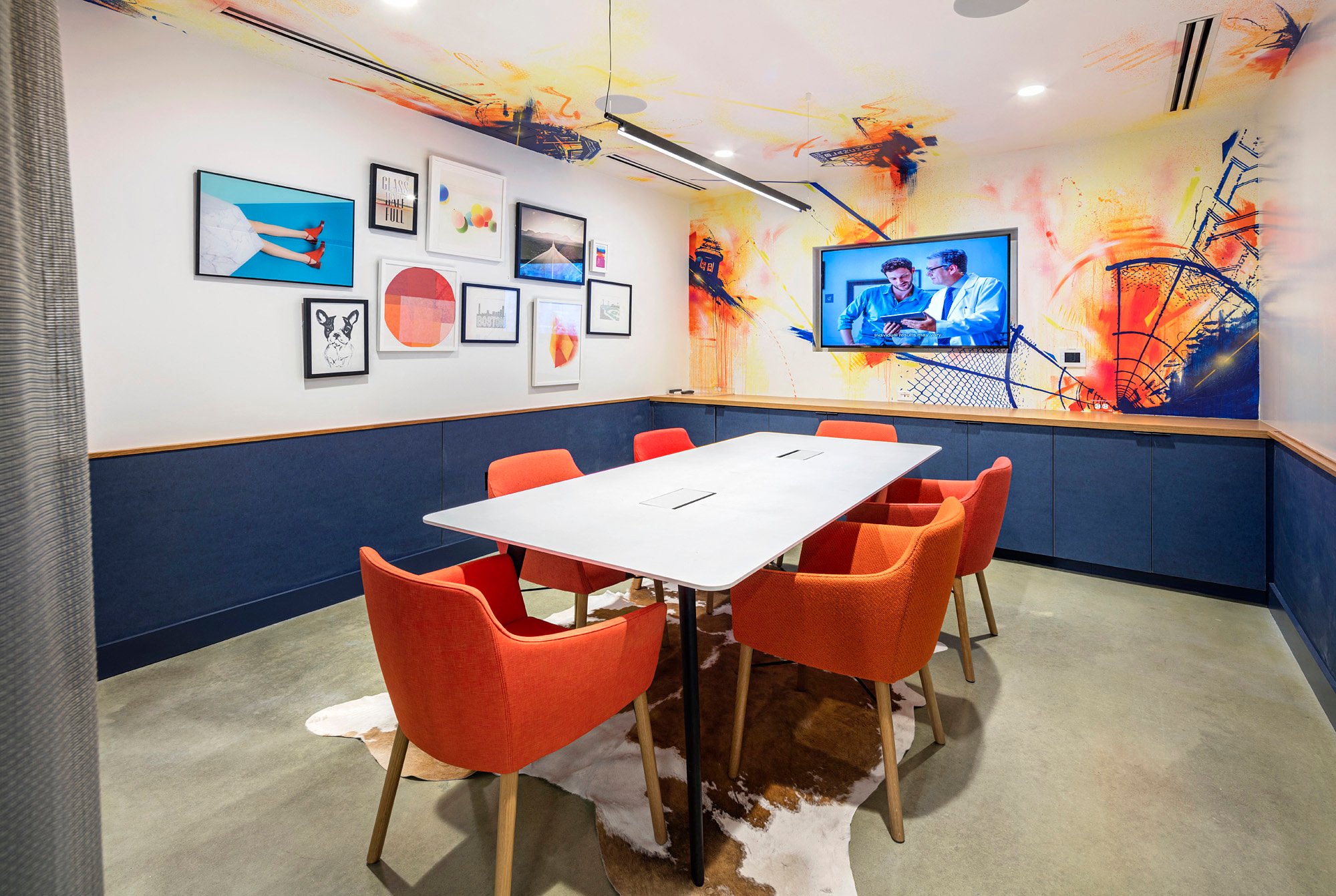a conference room with a white table and orange chairs and a tv on the wall