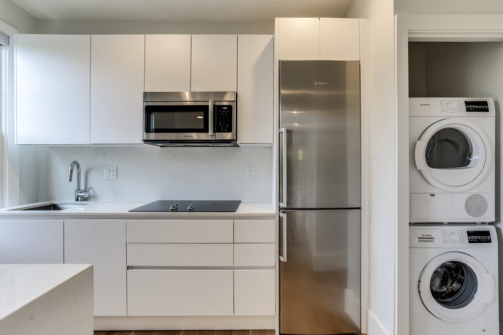 a white kitchen with a washer and dryer and a stainless steel refrigerator