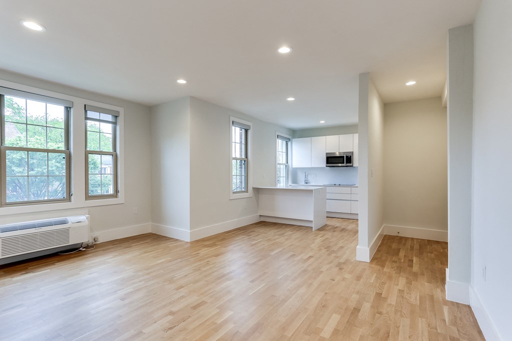 an empty living room with a kitchen in the background
