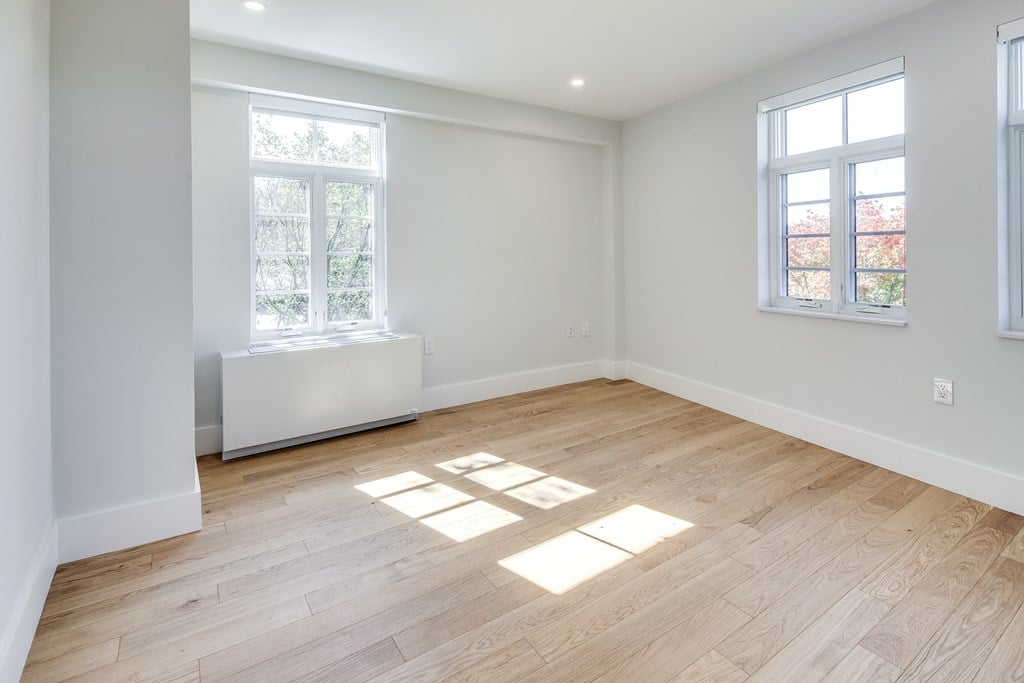 an empty room with wooden floors and two windows