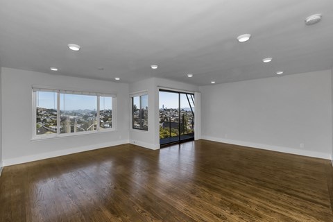 A spacious room with wooden floors and large windows overlooking a cityscape.