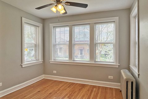 A room with a ceiling fan and three windows.