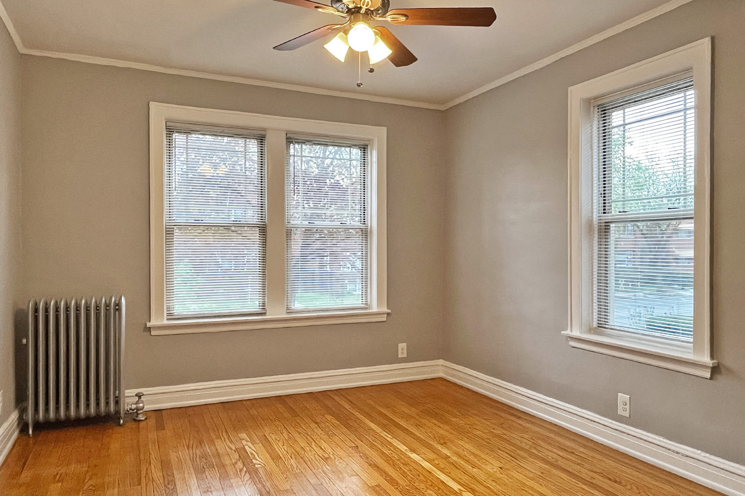 A room with a ceiling fan and two windows.