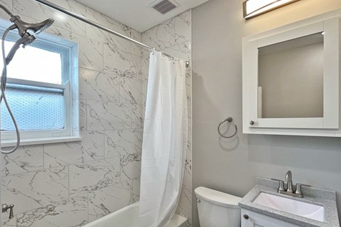 A white bathroom with a marble tile shower and a white toilet.