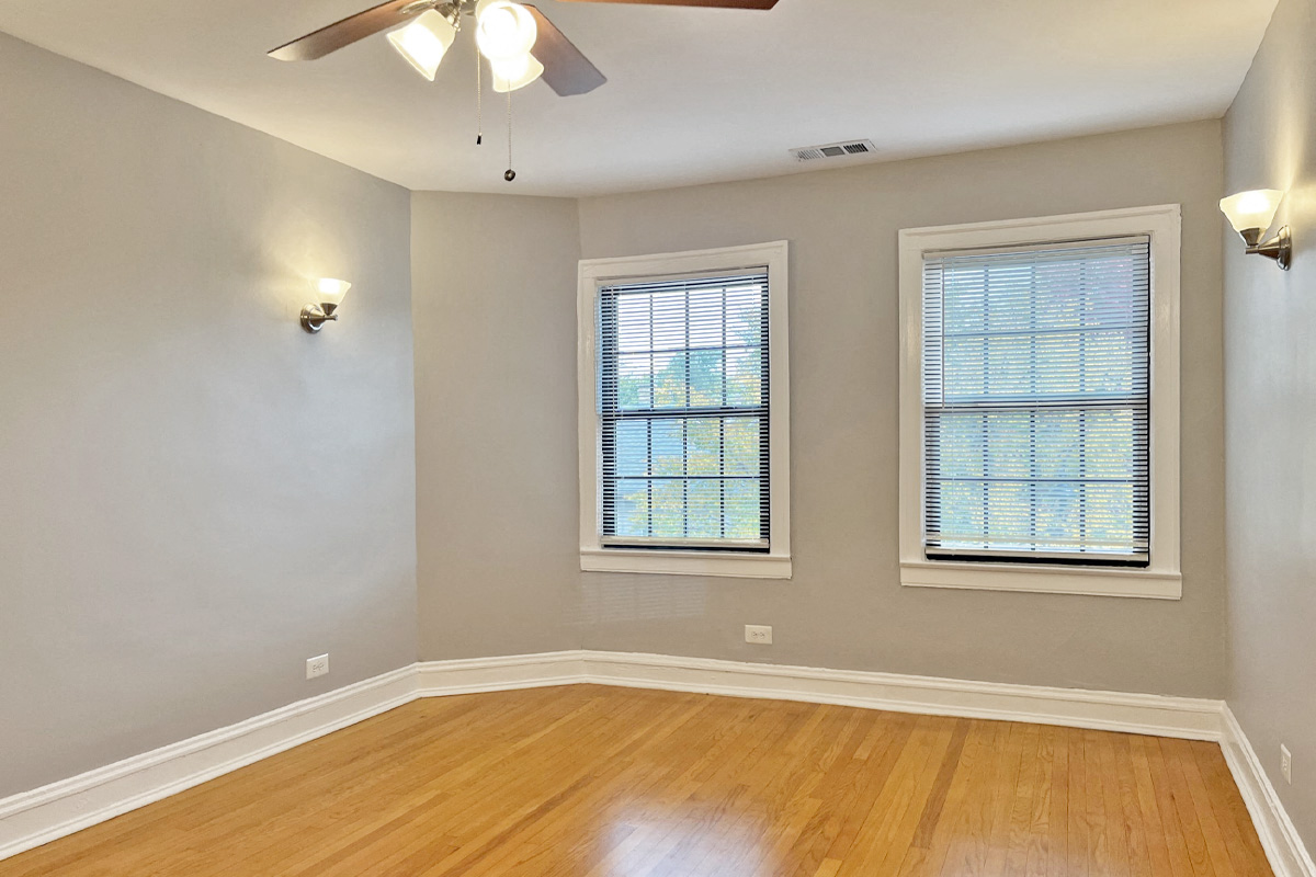an empty living room with a ceiling fan and two windows