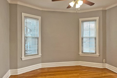 A room with a ceiling fan and two windows.