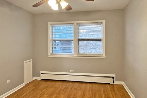 A room with a window, a ceiling fan, and a radiator on the floor.