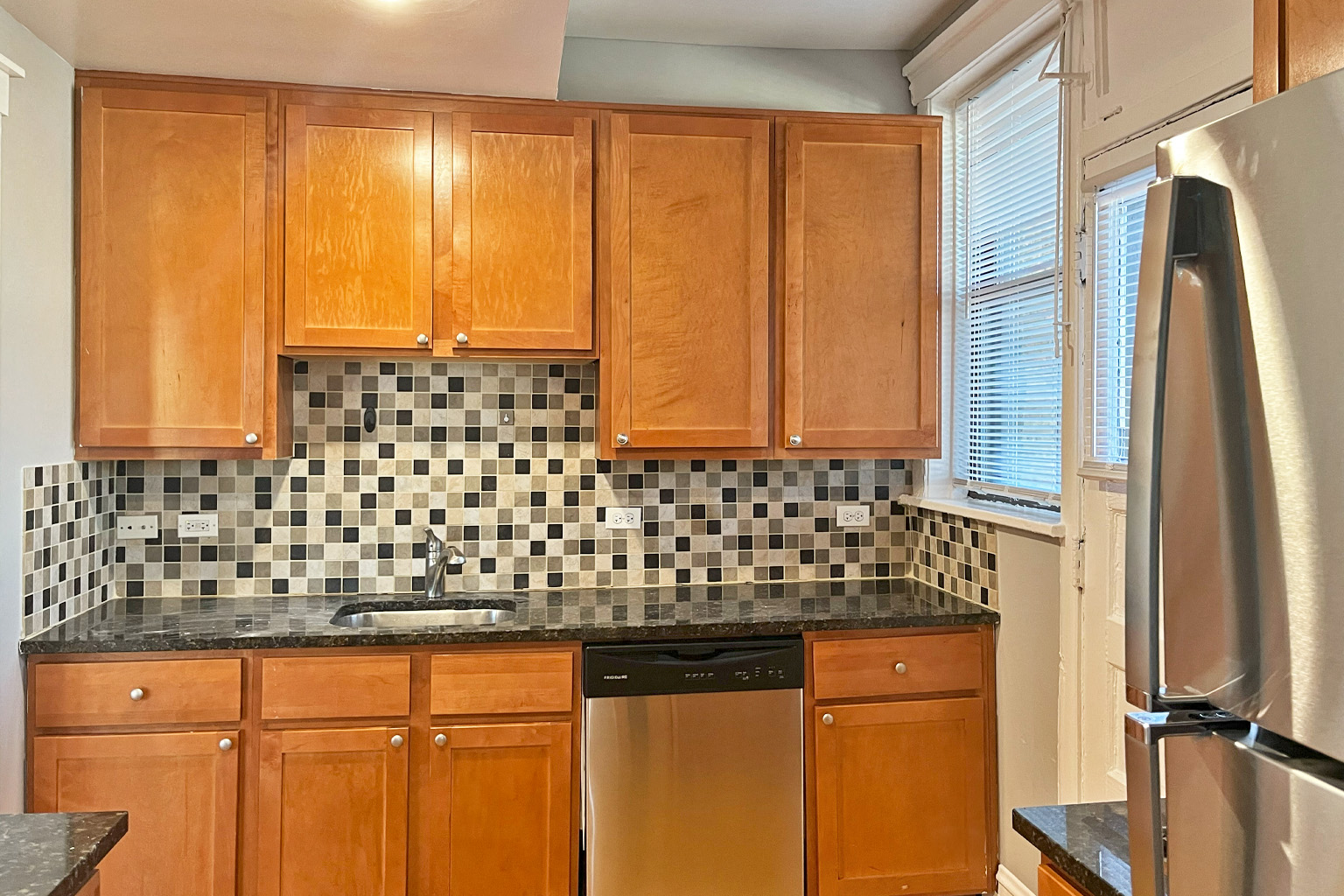 A kitchen with wooden cabinets and a black and white tiled backsplash.