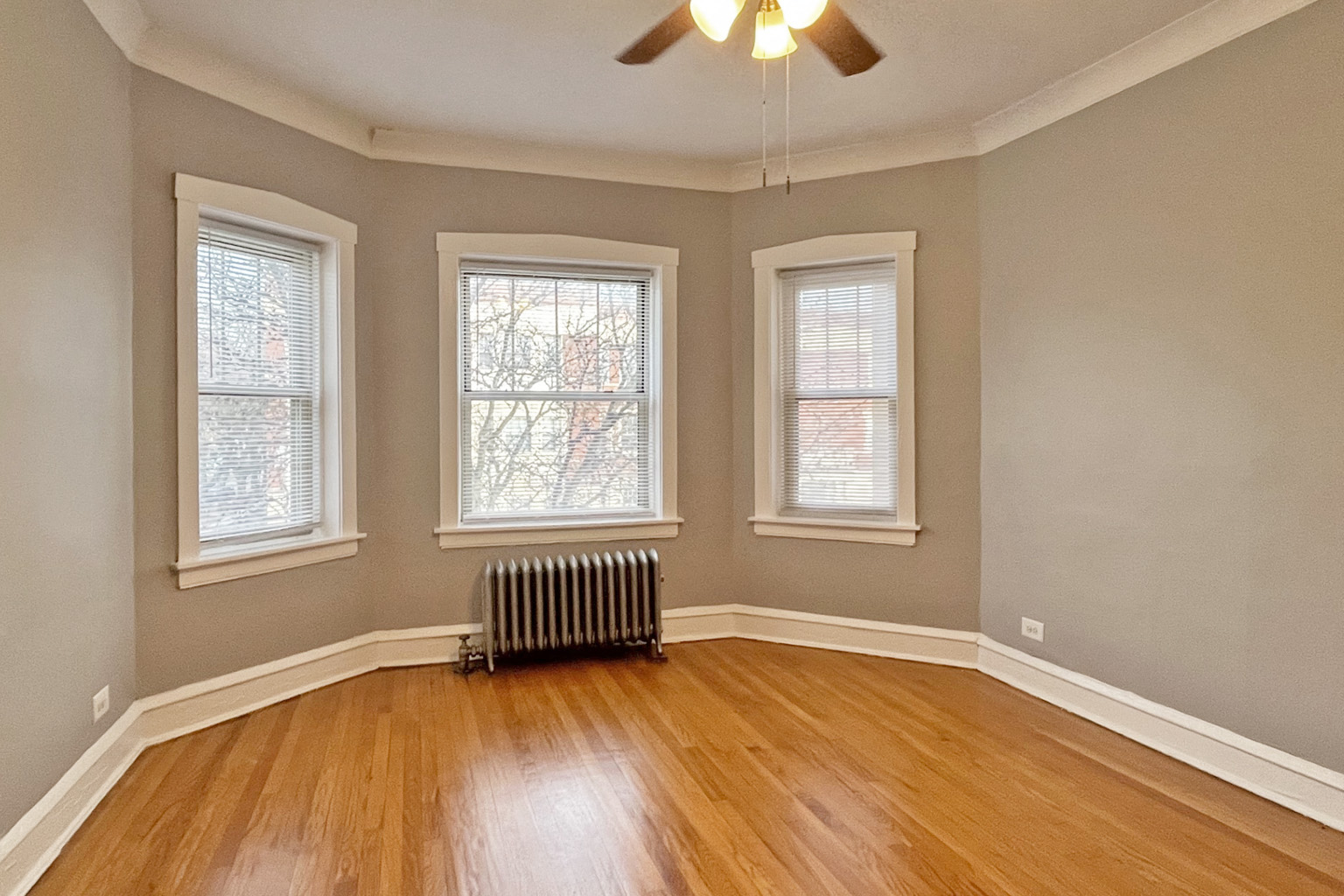 A room with wooden floors and three windows.