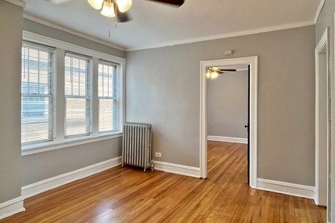 A room with a wooden floor, a ceiling fan, and a window with blinds.