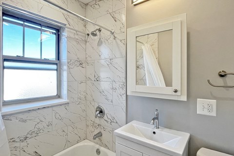 A white bathroom with a marble tile shower and a window.