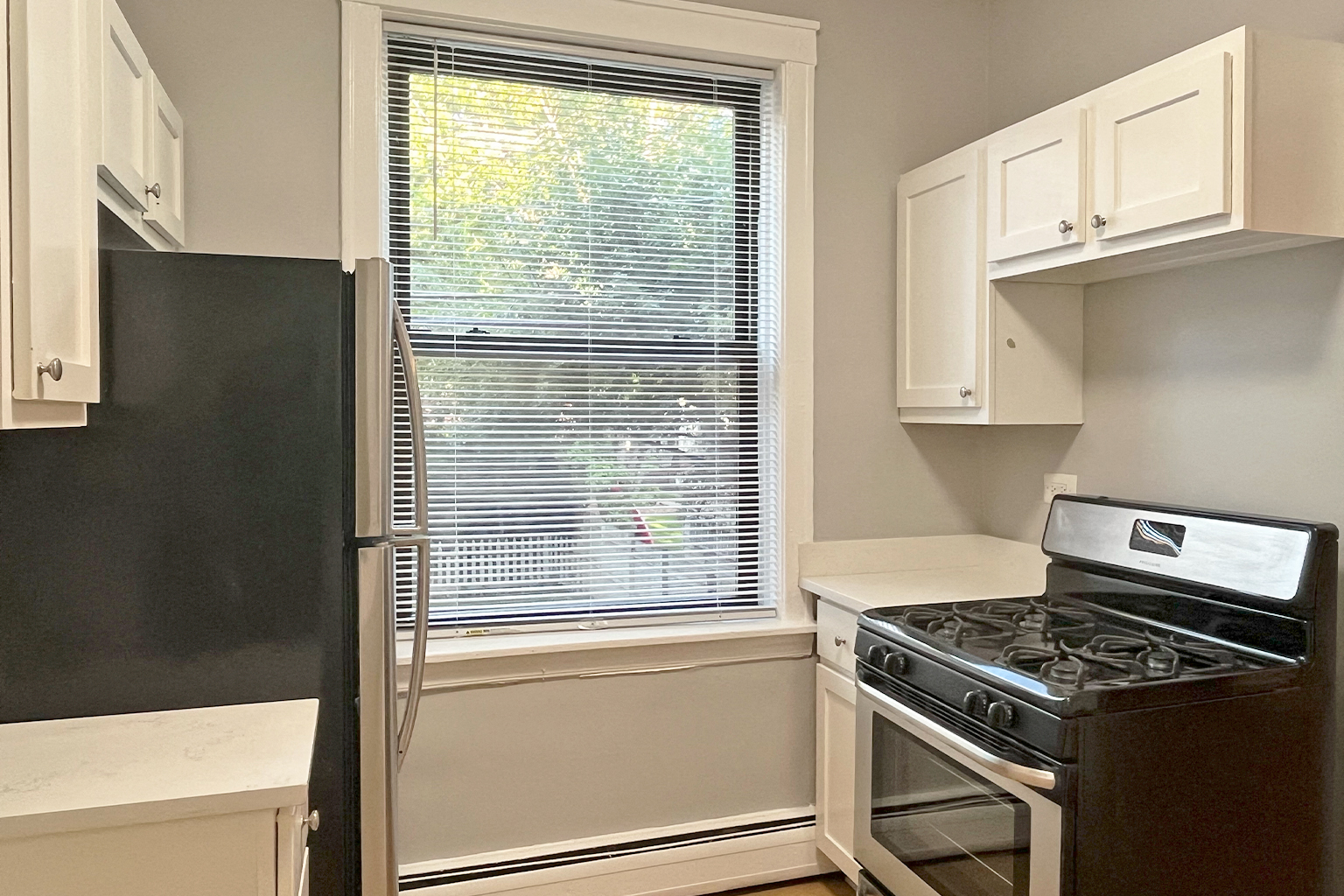 A black refrigerator is in a kitchen next to a window.