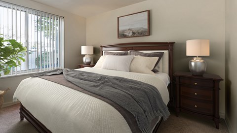 A bedroom with a large bed, a nightstand, and a window with blinds.