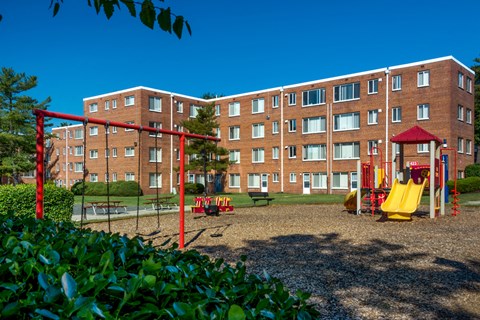A playground with a red swing set in front of a red brick apartment building.