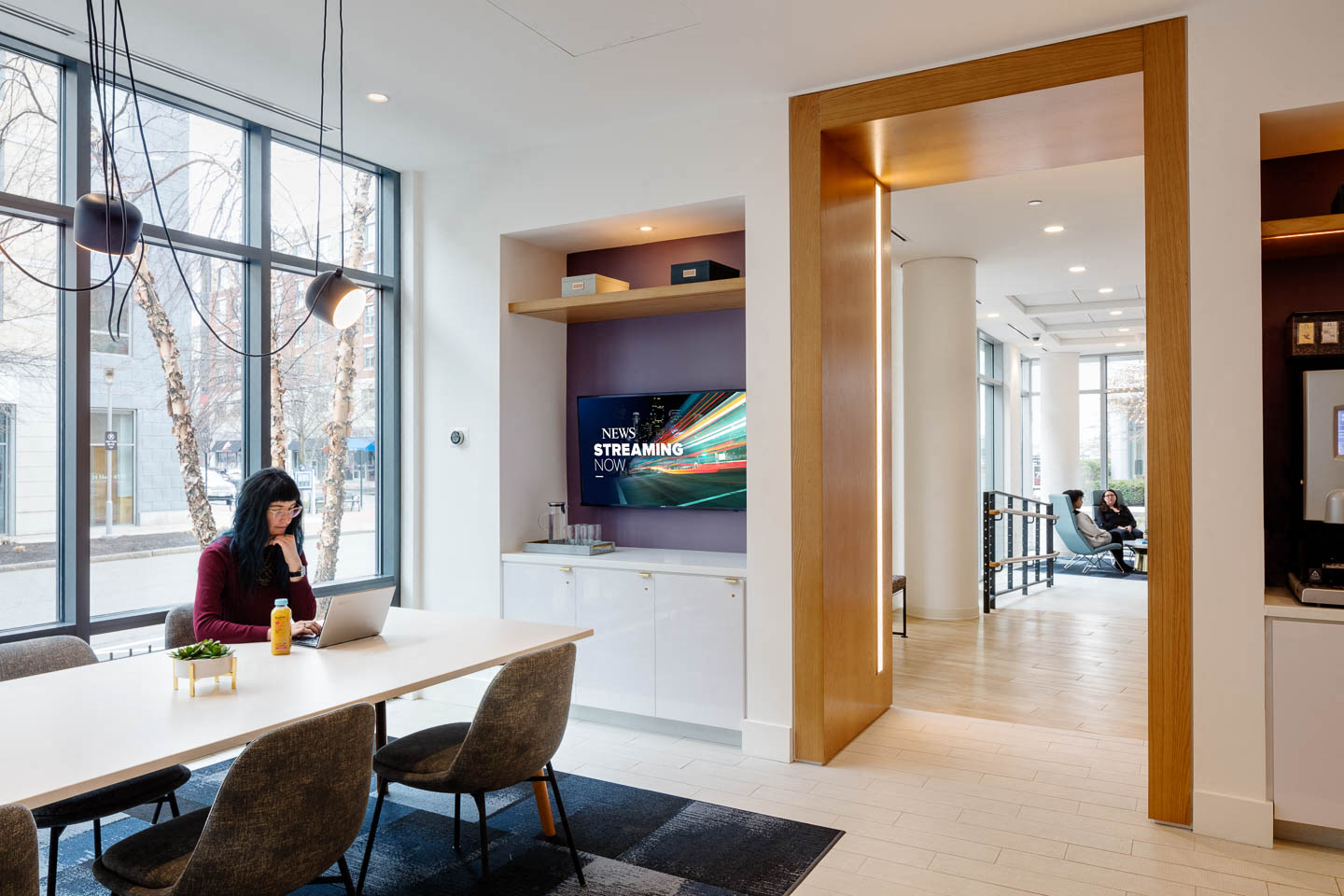 a woman sitting at a table with a laptop computer in a room with large windows