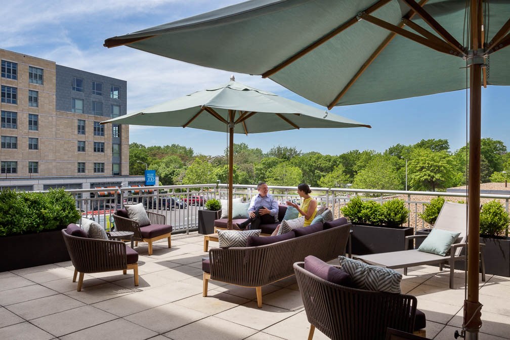 two people sitting on chairs under umbrellas on a rooftop patio