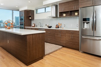San Francisco Apartments - Etta - Spacious Kitchen With Wood-style Cabinets and Flooring. Kitchen Also Includes Stainless Steel Appliances and a Kitchen Island with a White Countertop. - Photo Gallery 16