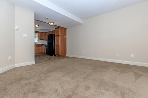 an empty living room with a kitchen in the corner