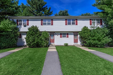 a white house with red shutters and a walkway in front of a lawn