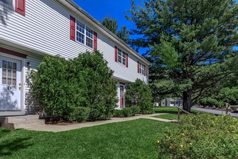 a side view of a white house with red window shutters and a sidewalk