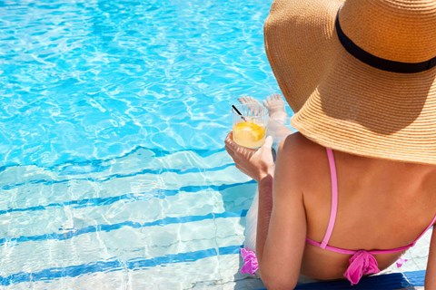 a woman in a sun hat drinking a drink by the pool
