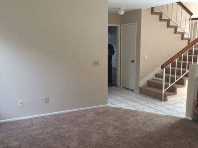 an empty living room with stairs and a door to a hallway