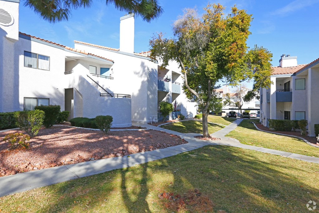 an apartment building with a sidewalk and trees in front of it