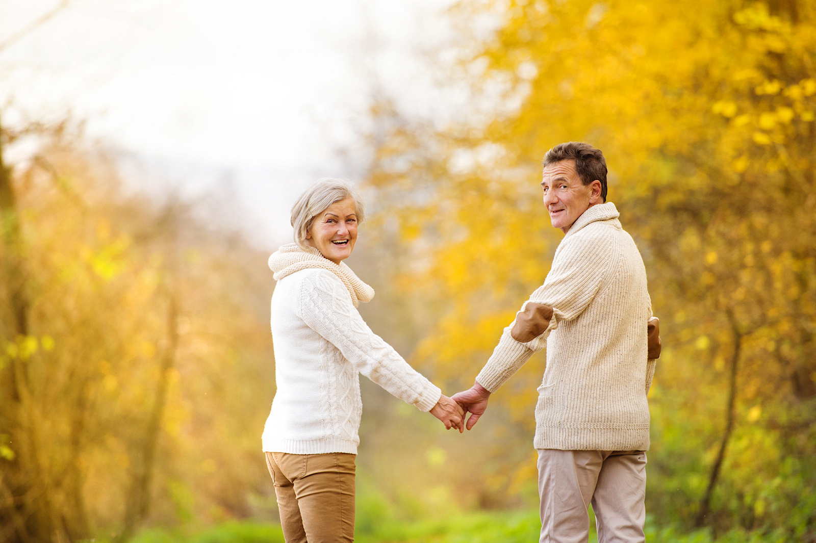 a man and woman holding hands while walking in the park