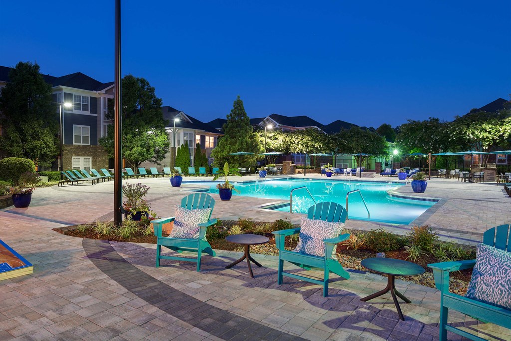a swimming pool with chairs and tables around it at night