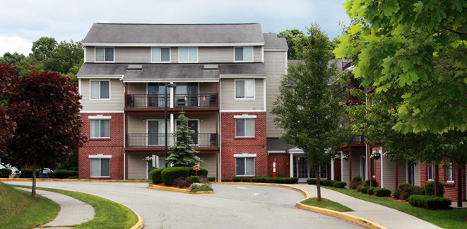 an apartment building with a driveway and trees in front of it