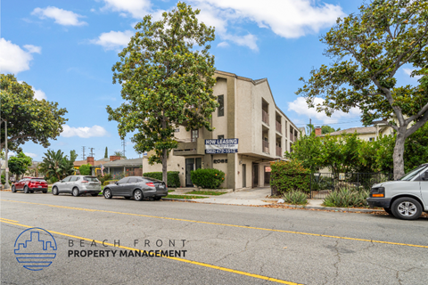 A building with the sign "BEACH FRONT PROPERTY MANAGEMENT" is surrounded by trees and cars on the street.