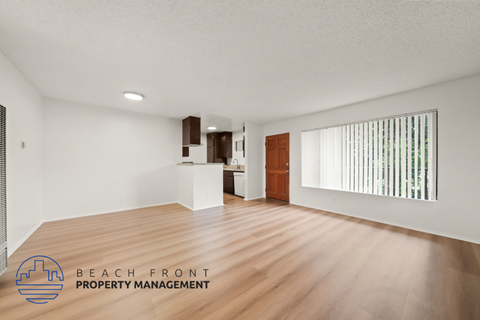 A spacious room with wooden flooring and a logo for Beach Front Property Management in the corner.