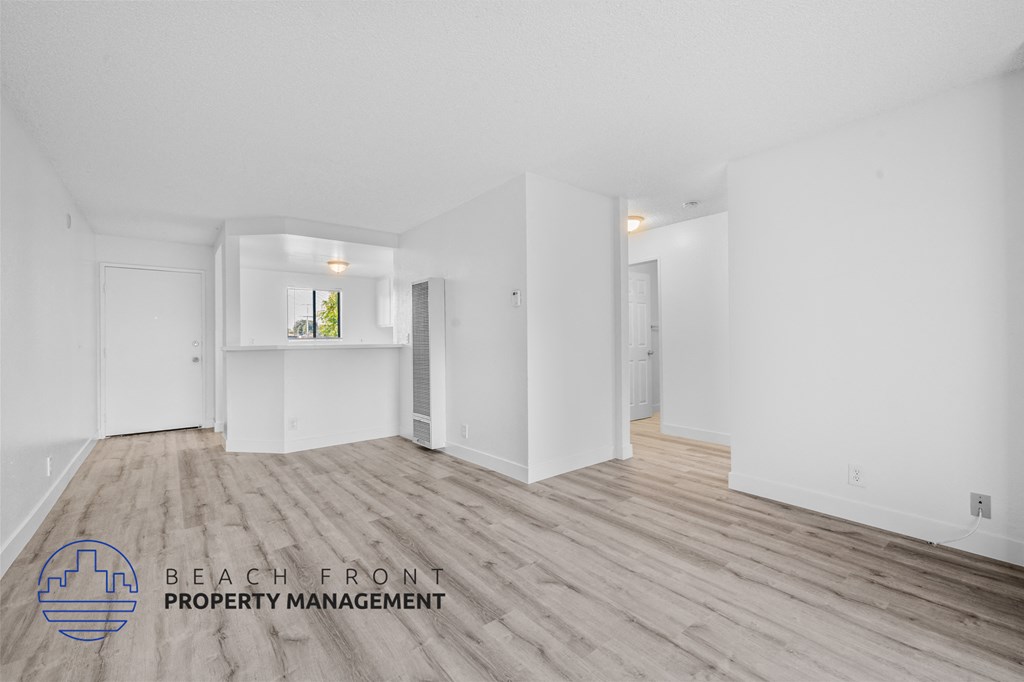 a living room and kitchen with white walls and wood flooring