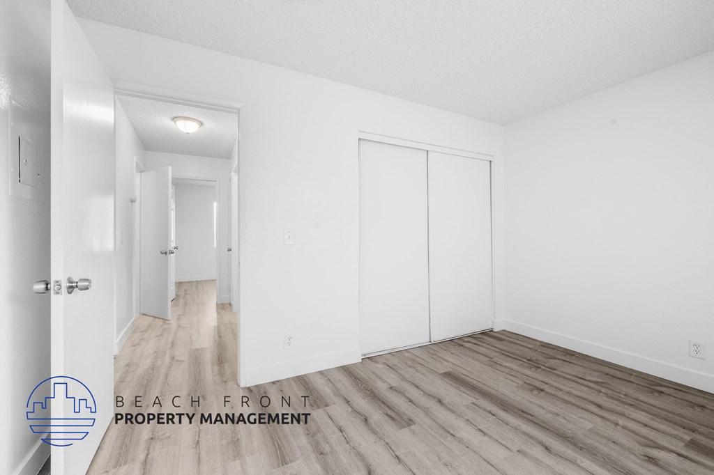 a bedroom with white walls and wood flooring and white closets