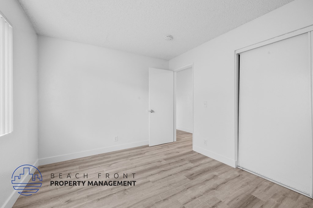 a bedroom with white walls and wood flooring and a closet