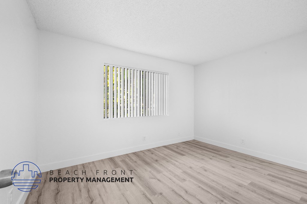 a spacious living room with white walls and wood flooring and a window