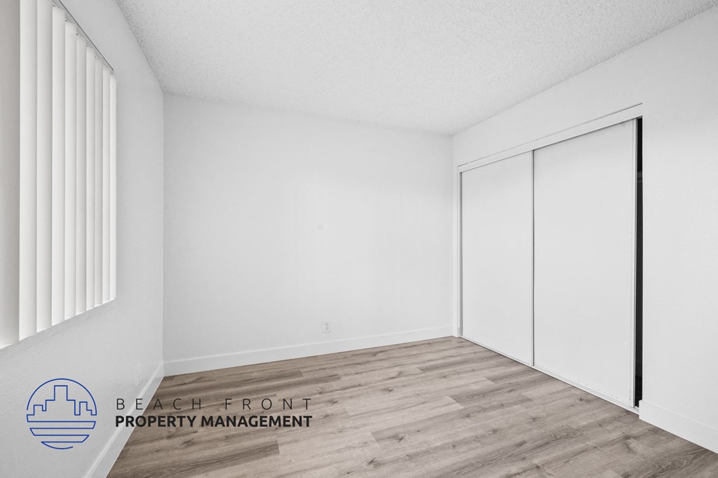 a bedroom with white walls and wood flooring and white closet doors