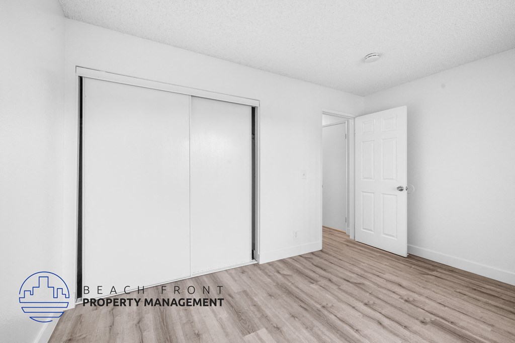 a bedroom with white walls and wood flooring and white closet doors