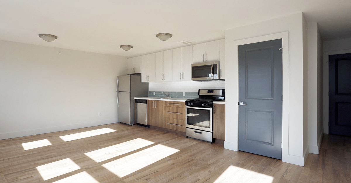 Open layout living room and kitchen with hardwood floors, stainless steel appliances, wooden and white cabinets
