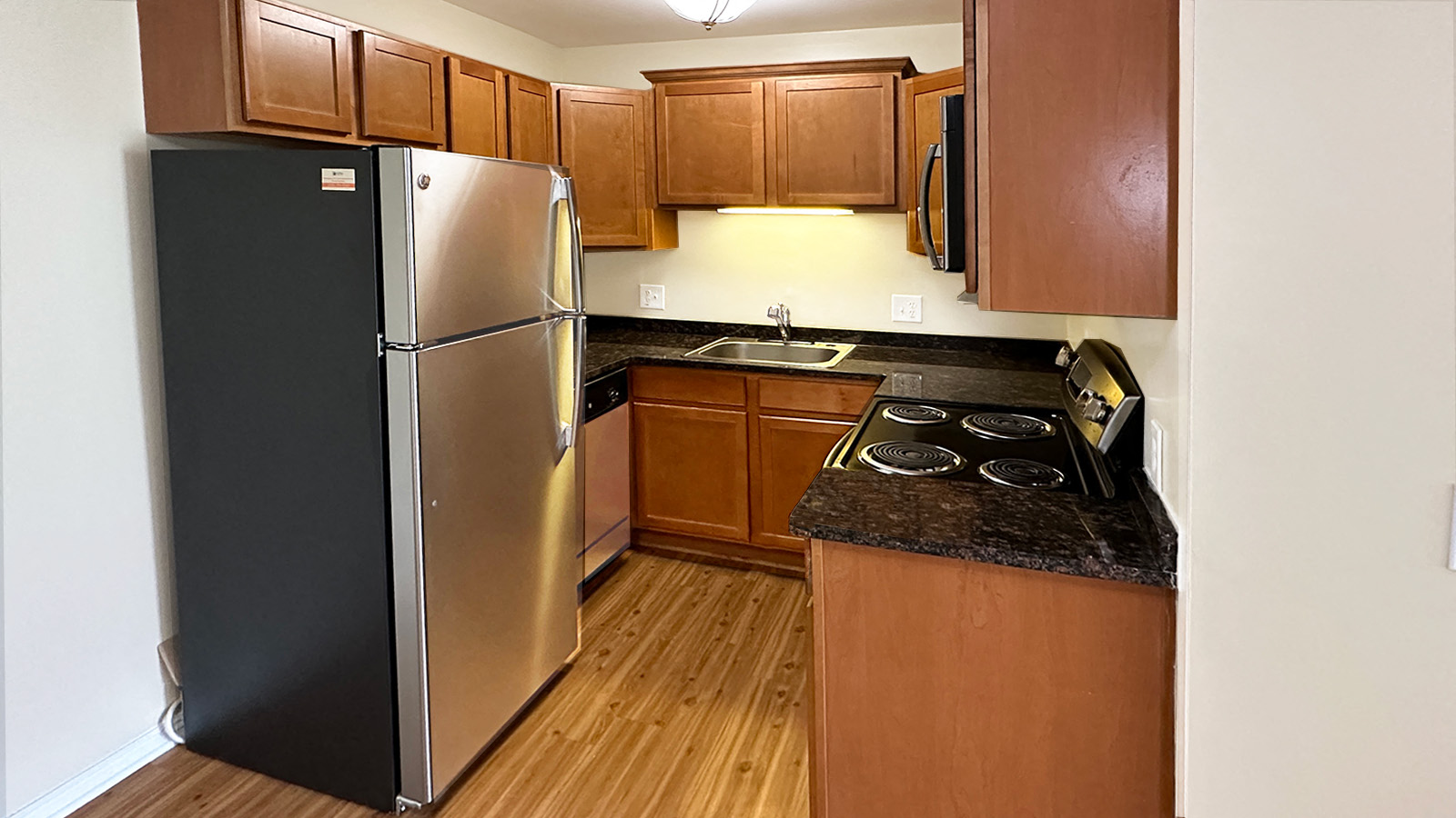 A black refrigerator is in a kitchen with wooden cabinets.