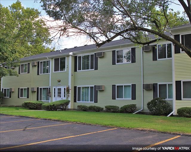 a large apartment building with a lawn and trees