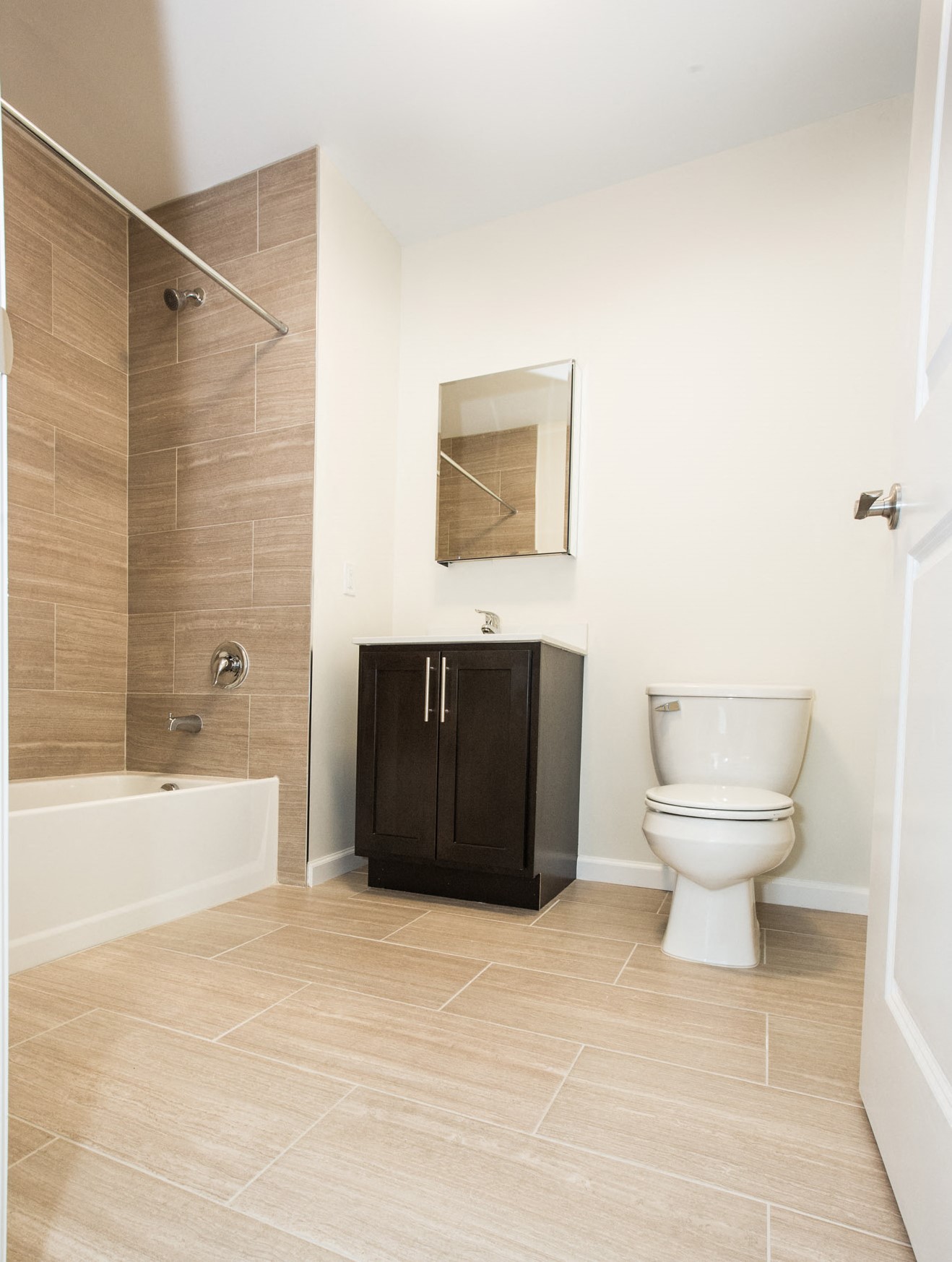 bathroom with beige tile floor and shower wall & dark wooden cabinets