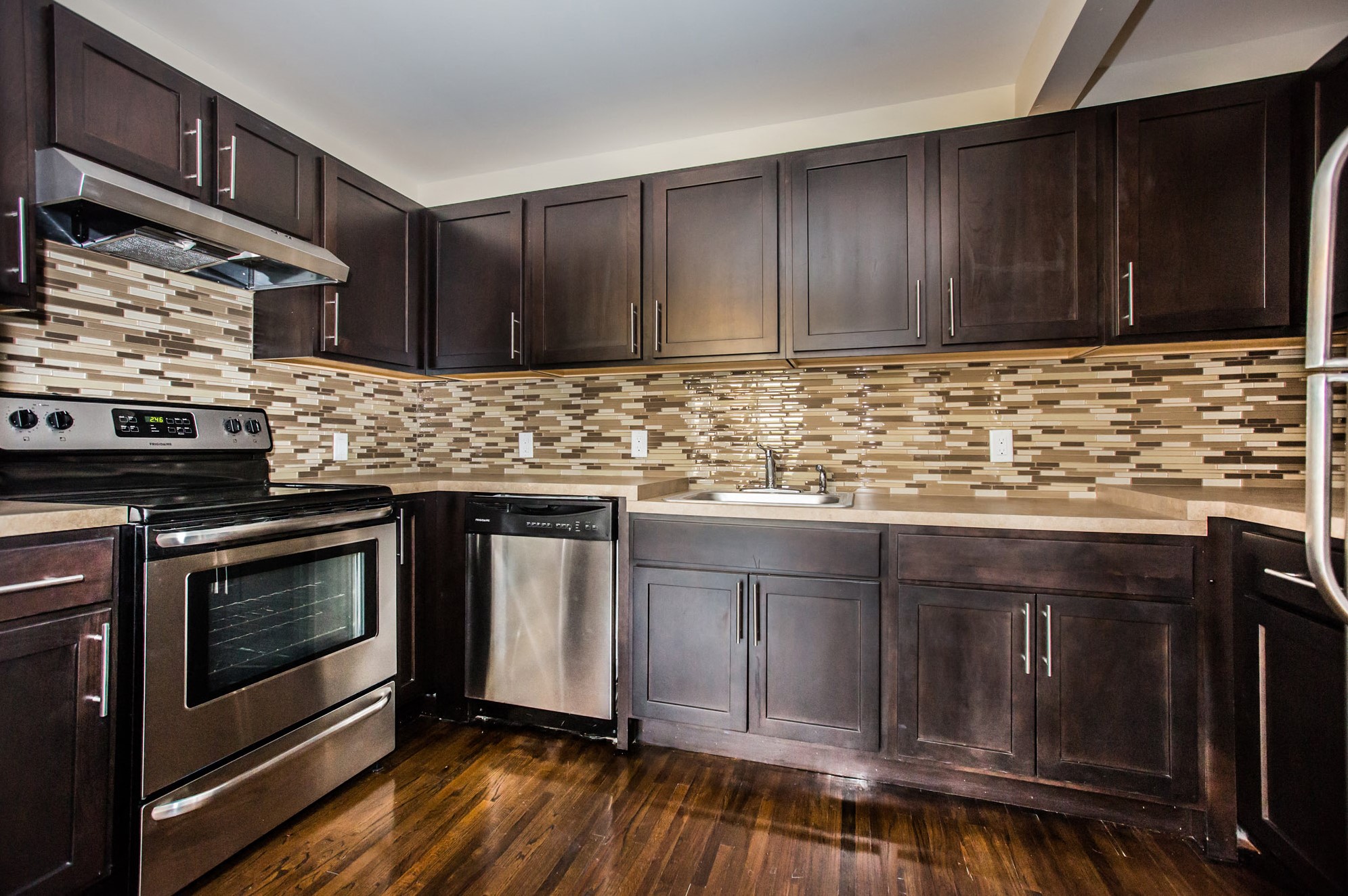 Kitchen with hardwood floors, dark wooden cabinets, tile patterned back splash and stainless steel appliances