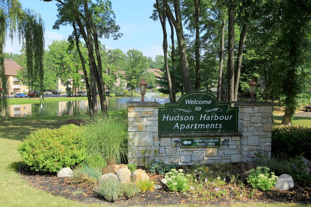 a sign for hudson harbour apartments in front of a lake and trees
